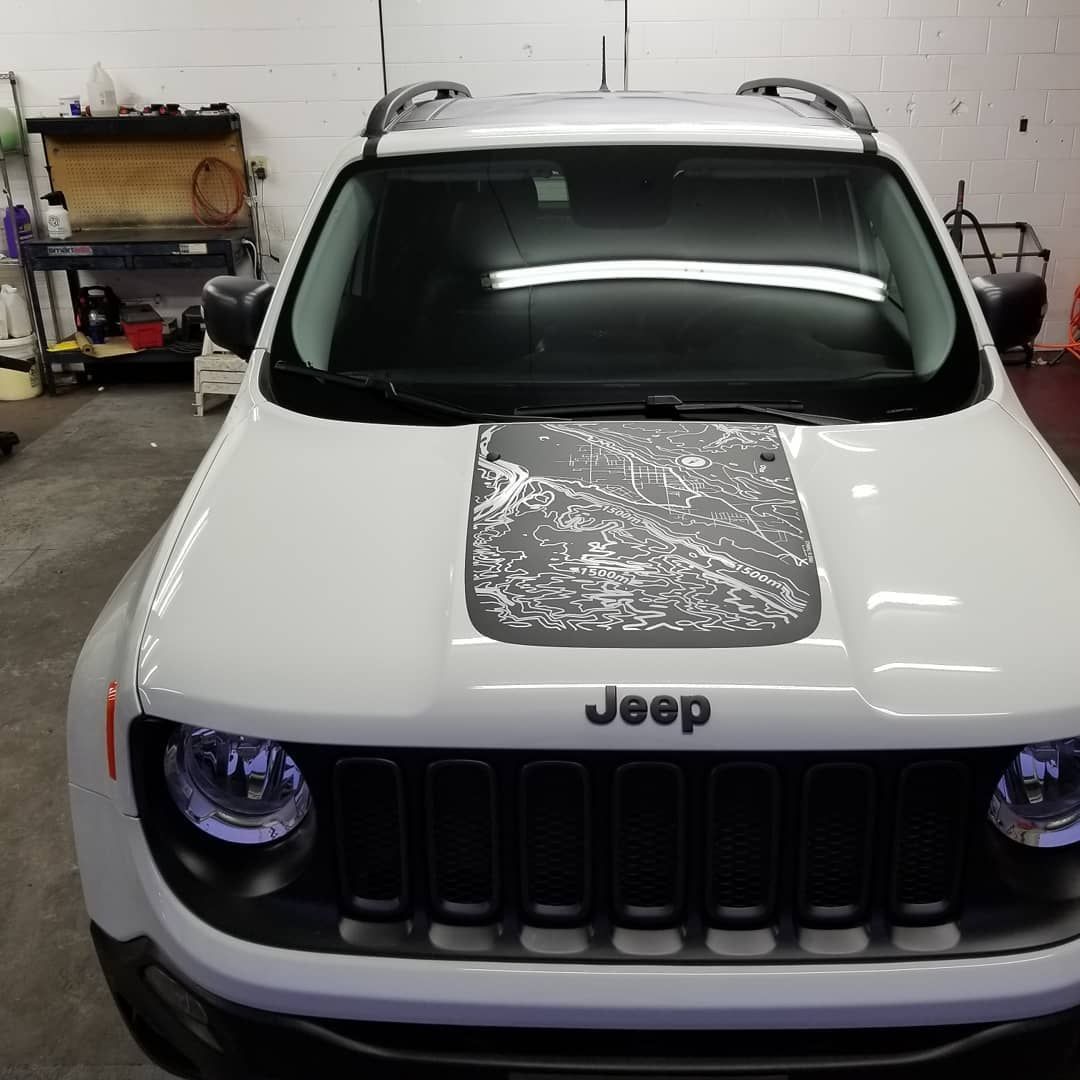 White Jeep Renegade with a black grill, a hood decal, and the Jeep logo.