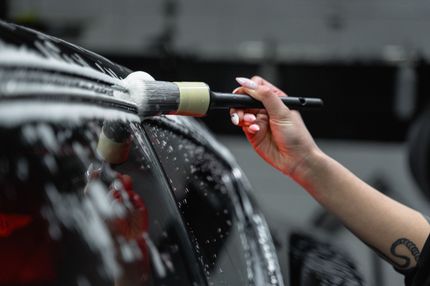 A person washes a black car with a brush and soapy water, close-up.