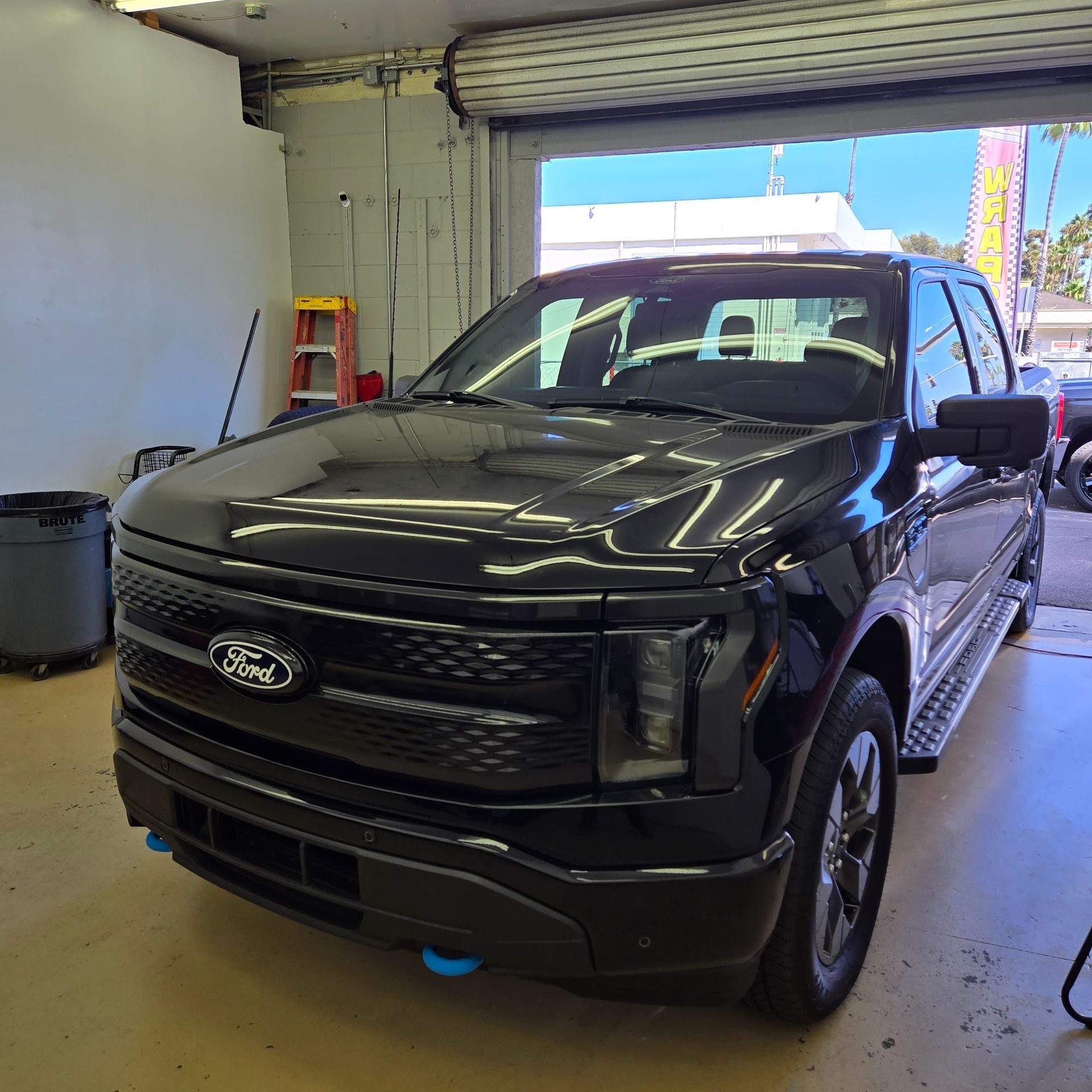 Black Ford F-150 Lightning electric truck parked inside a garage with the door open.