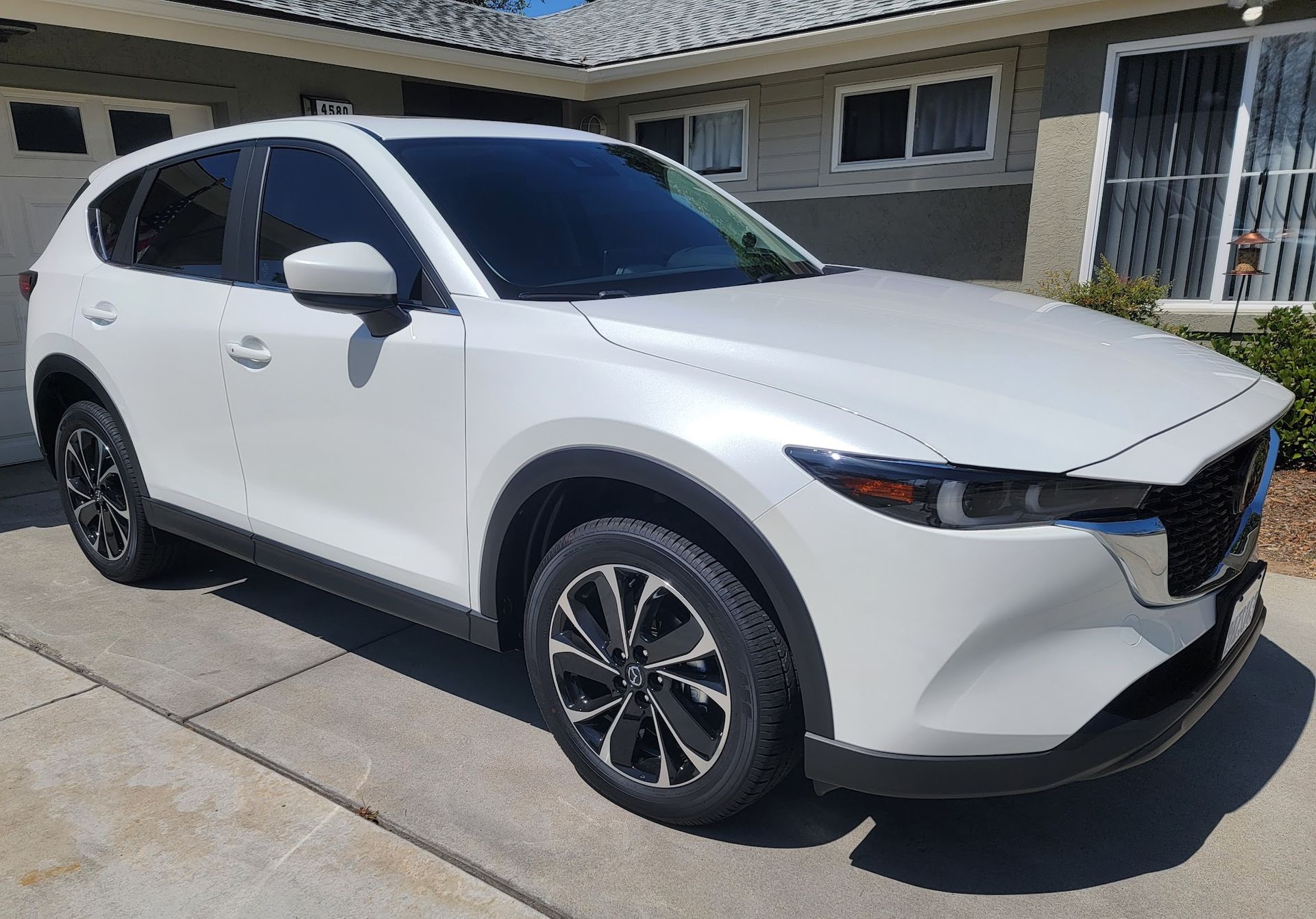 White Mazda CX-5 SUV parked on a driveway in front of a house on a sunny day.