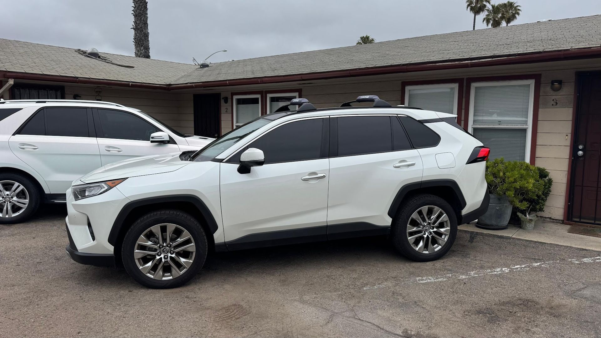 White Toyota SUV parked in front of a building, next to a silver SUV. Cloudy day.