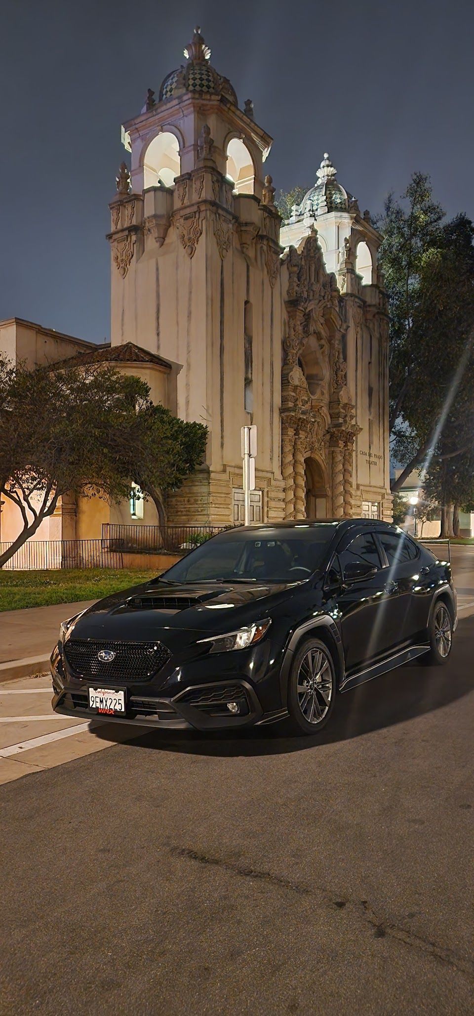 Black car parked in front of a large building with ornate towers at night.