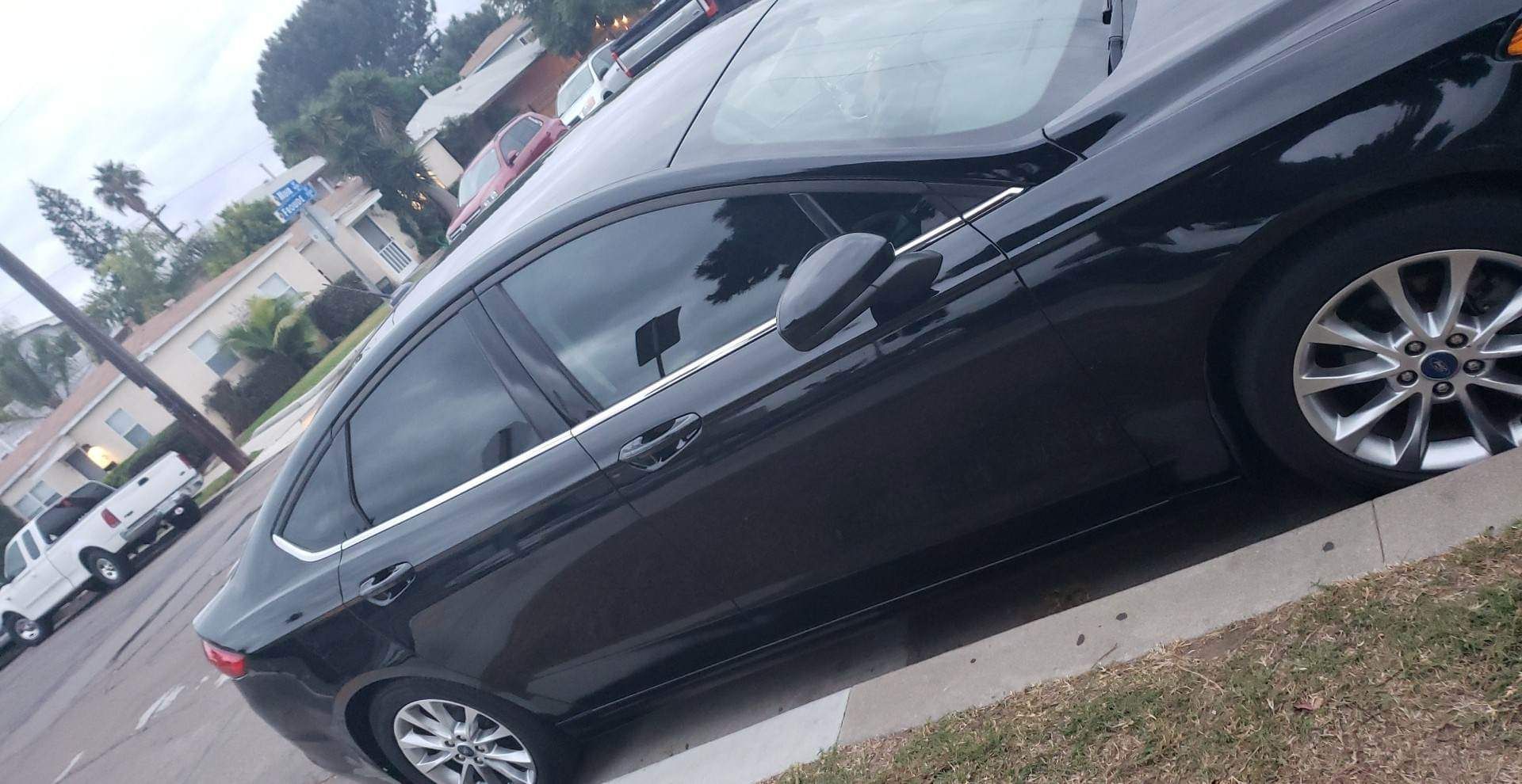 Black Ford sedan parked on a street next to a curb. Cloudy day.