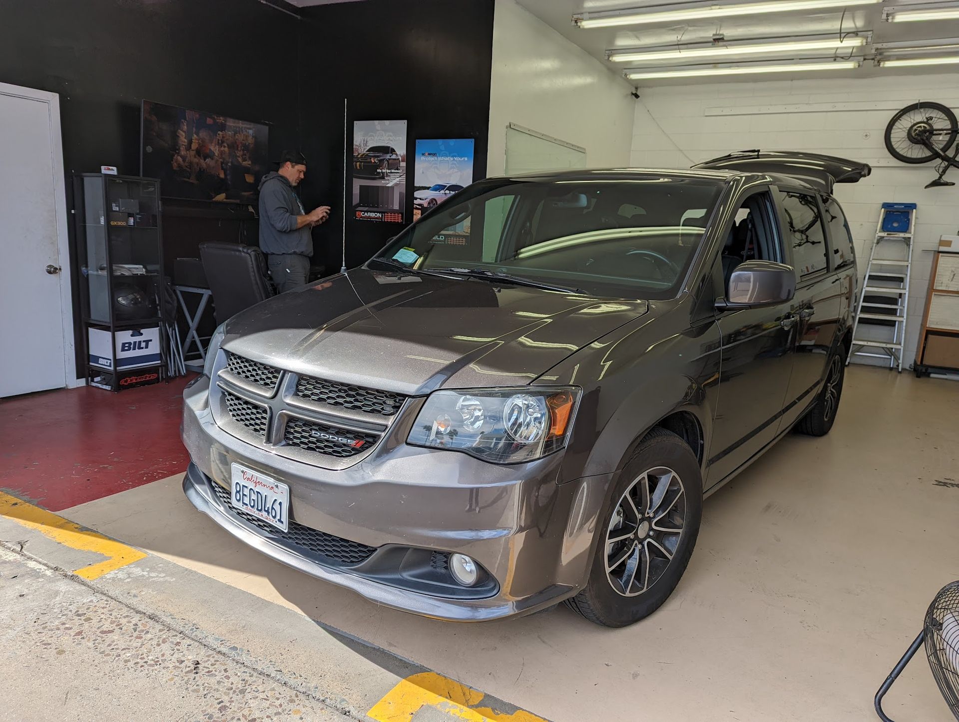 Gray Dodge Grand Caravan parked in a garage with a person in the background.
