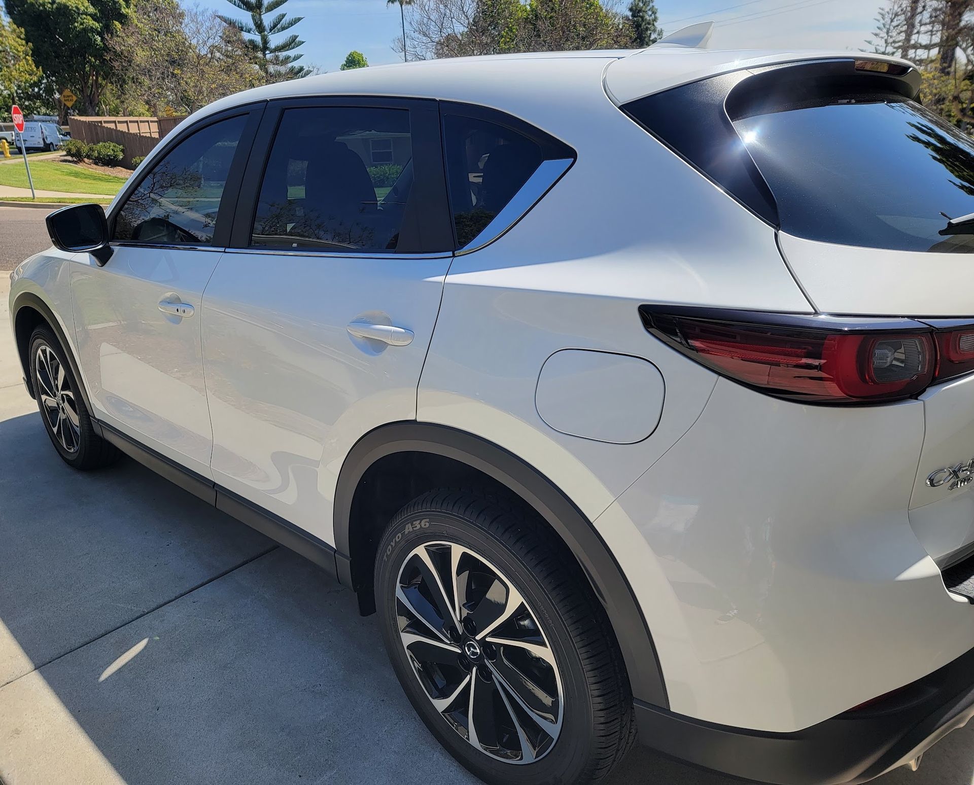 White Mazda CX-5 SUV parked on a driveway, with tinted windows and black wheels, under a blue sky.