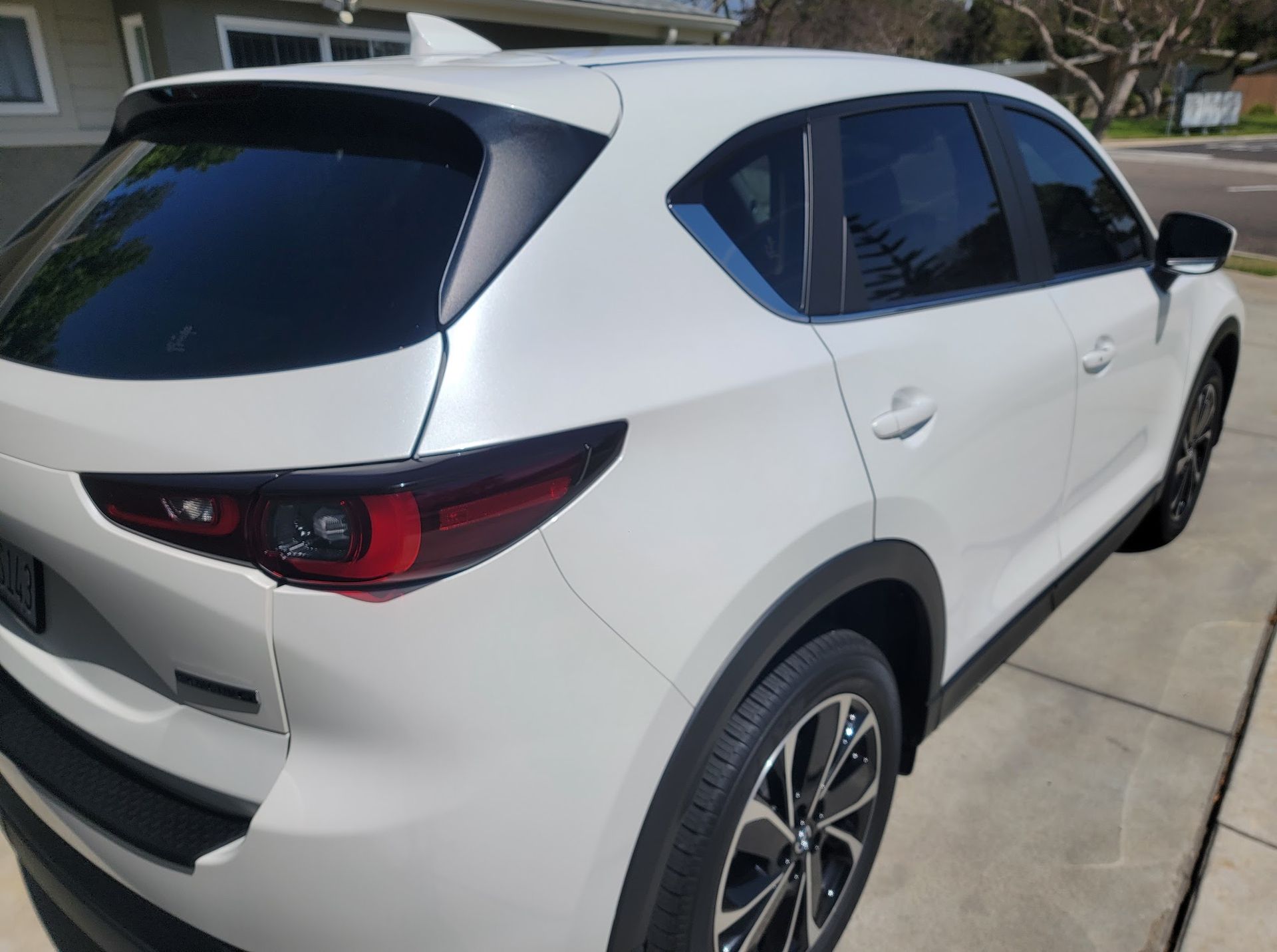 White Mazda CX-5 SUV parked on a paved driveway, side view. Black accents and tinted windows.