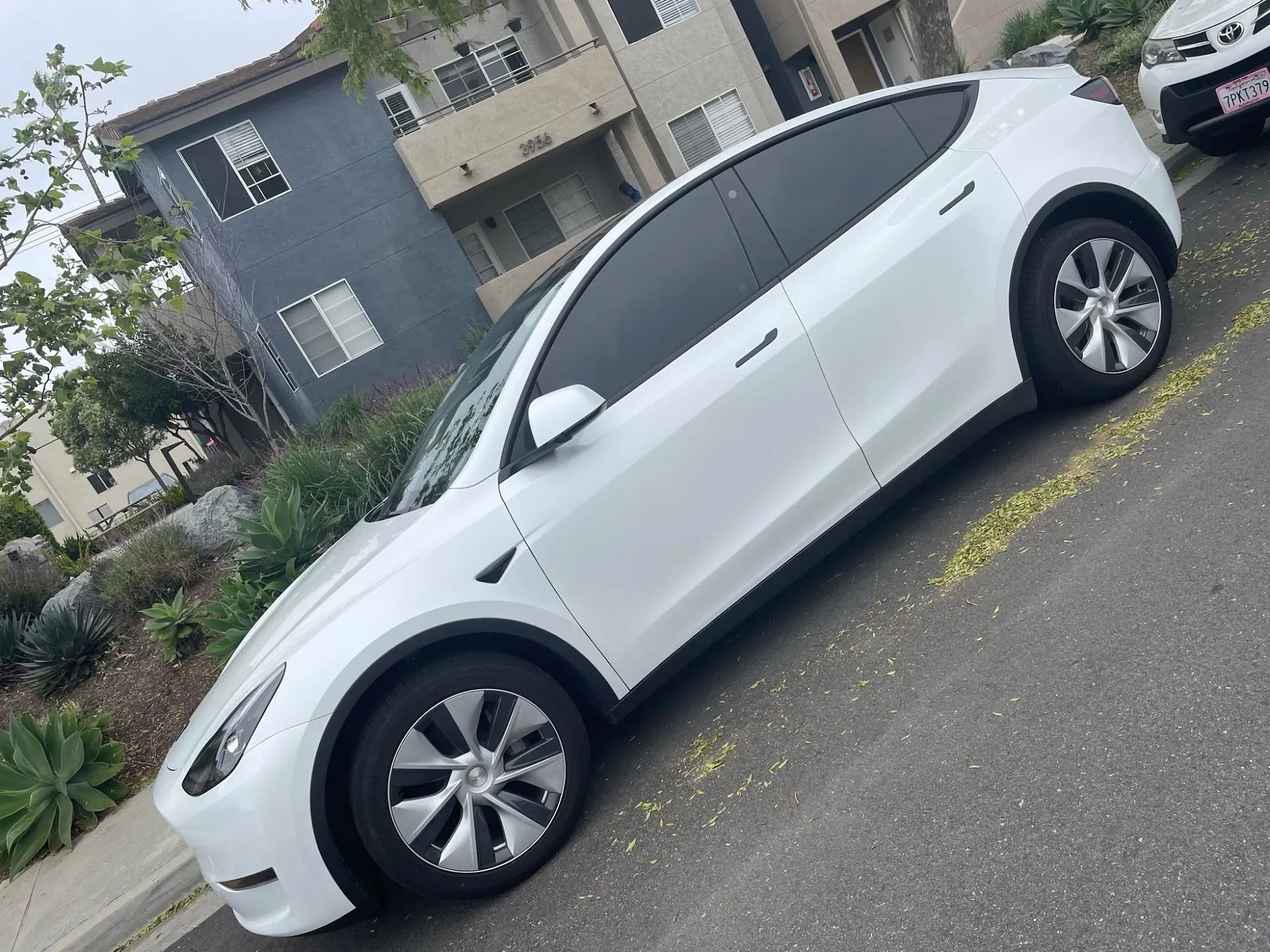White Tesla Model Y parked on a street with tinted windows.