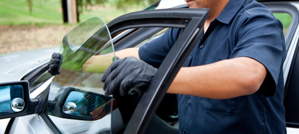 A person wearing gloves uses a tool to install a window in a car door.