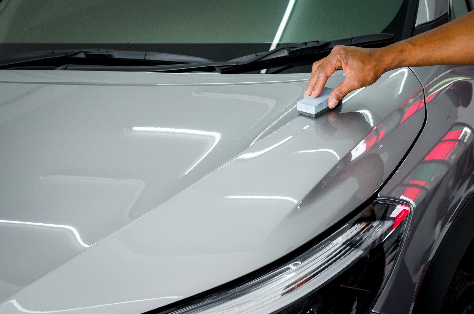 Person applying ceramic coating to a gray car hood.