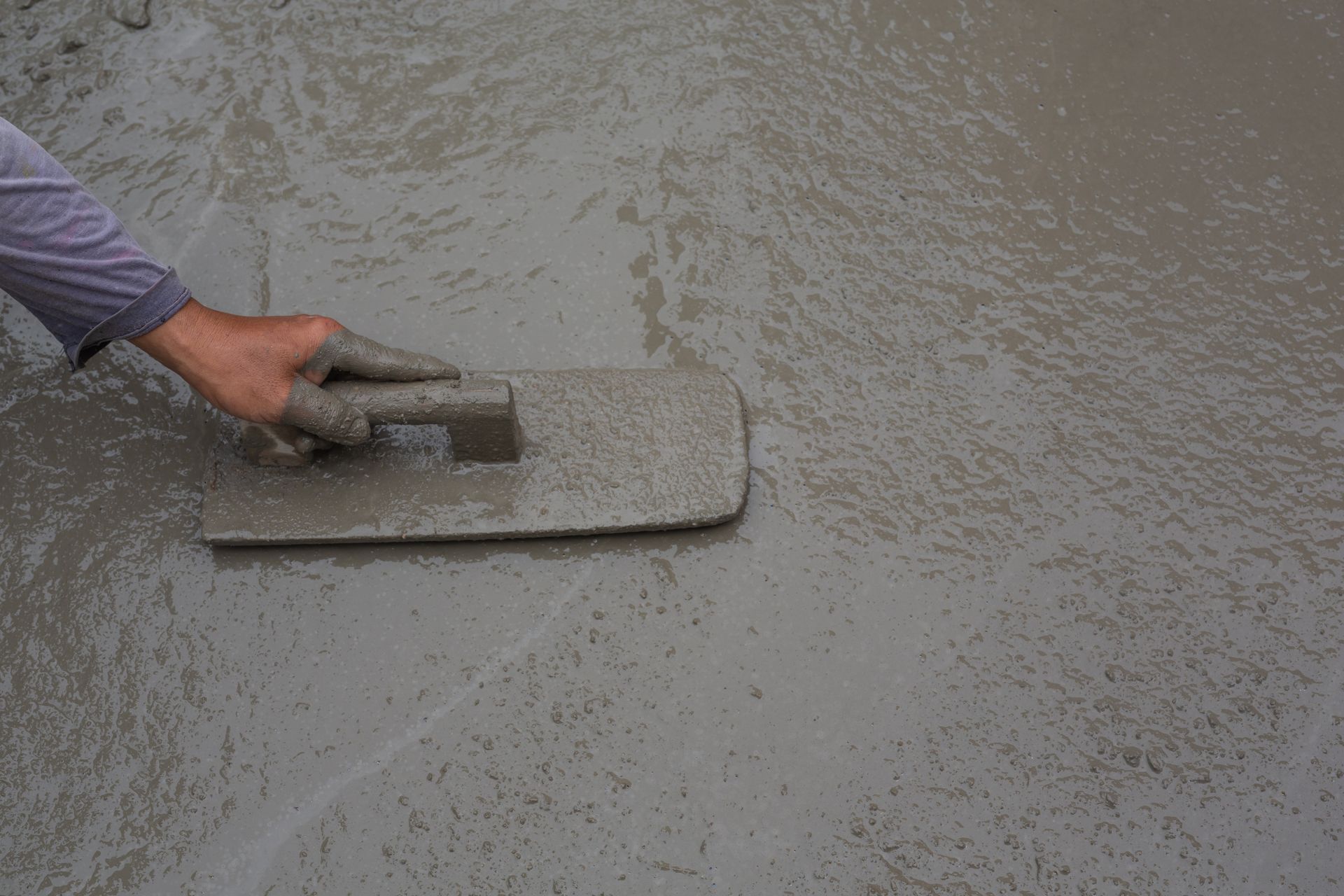 A person is using a trowel to smooth concrete.