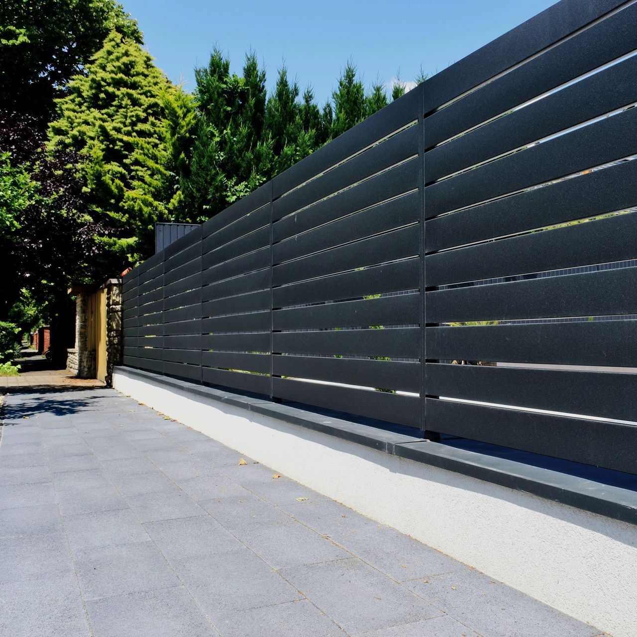 A black fence along a driveway with trees in the background