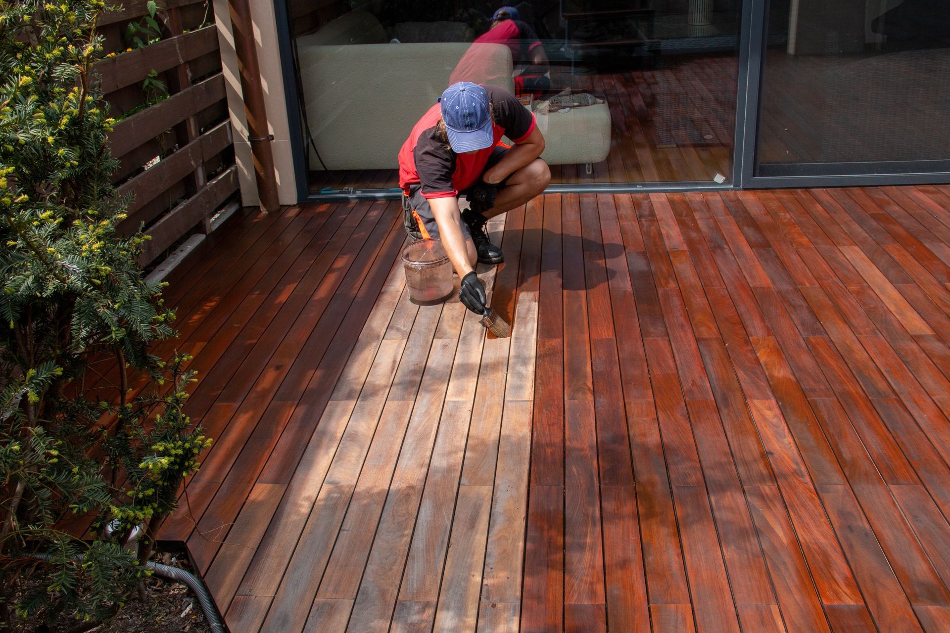 A man is painting a wooden deck with a brush.