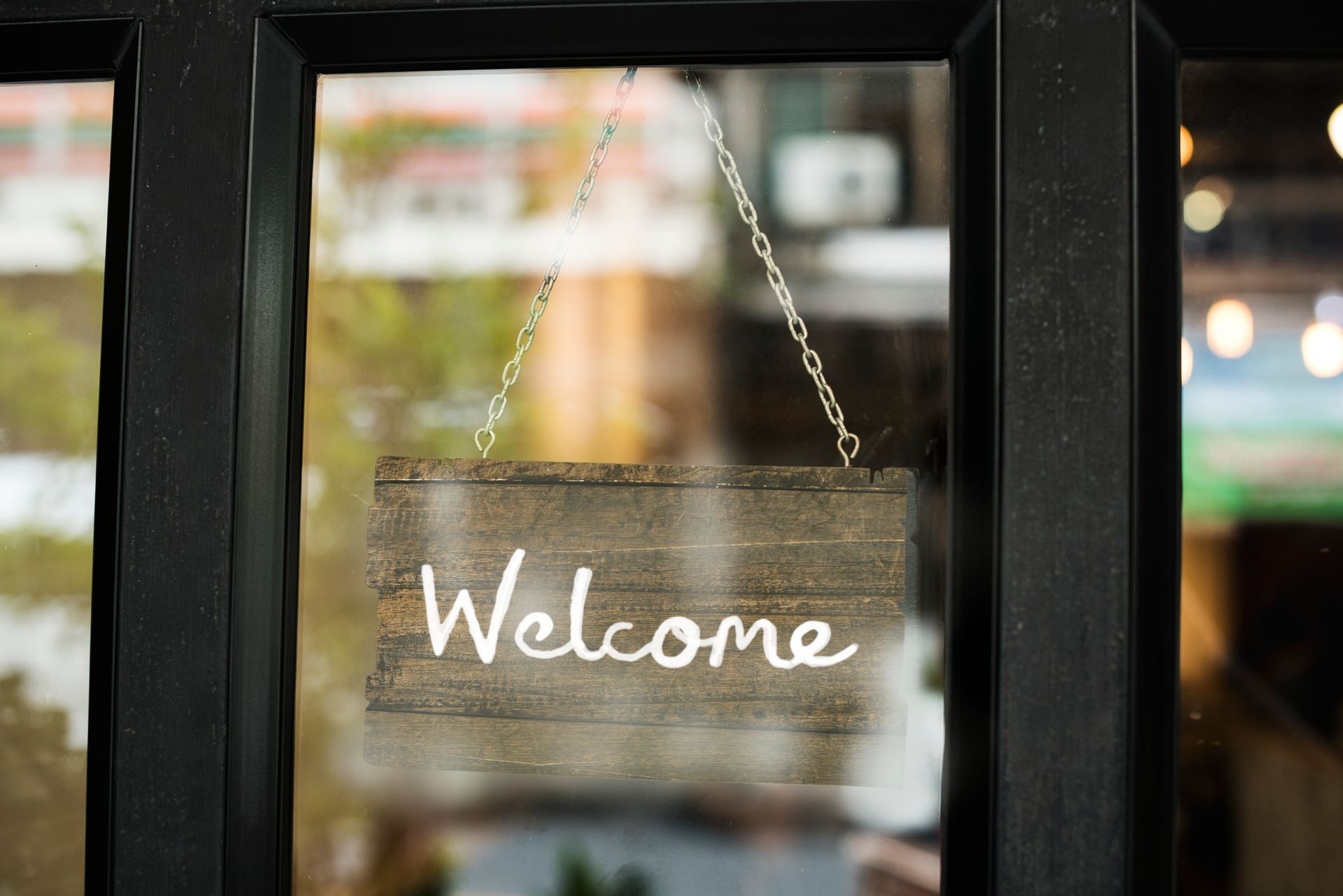 A welcome sign is hanging on a chain in a window.