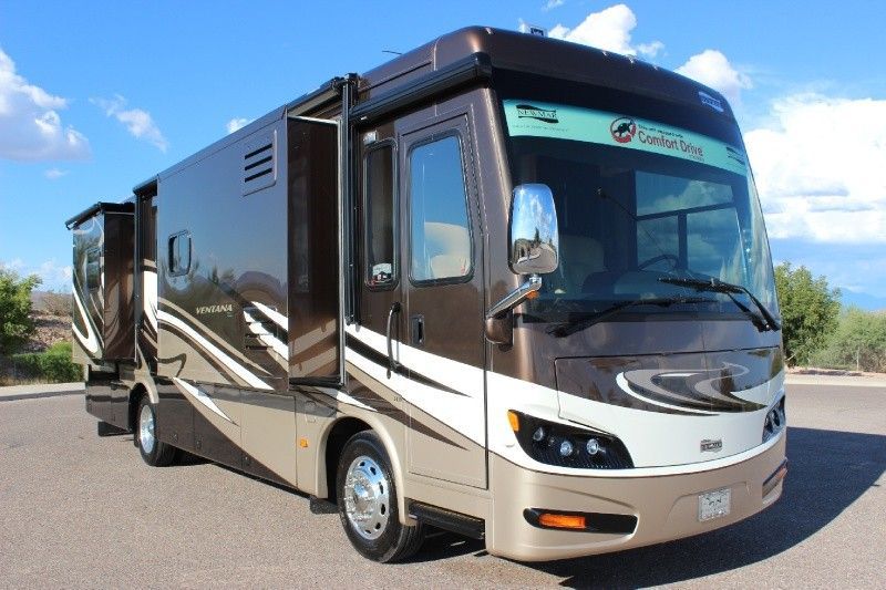 A brown and beige Class A motorhome parked on an asphalt lot under a blue sky.