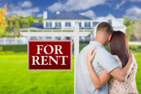 A couple with arms around each other looks at a house with a red