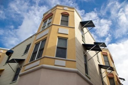 A low-angle view of a multi-story, yellow building with modern black metal awnings against a cloudy blue sky.