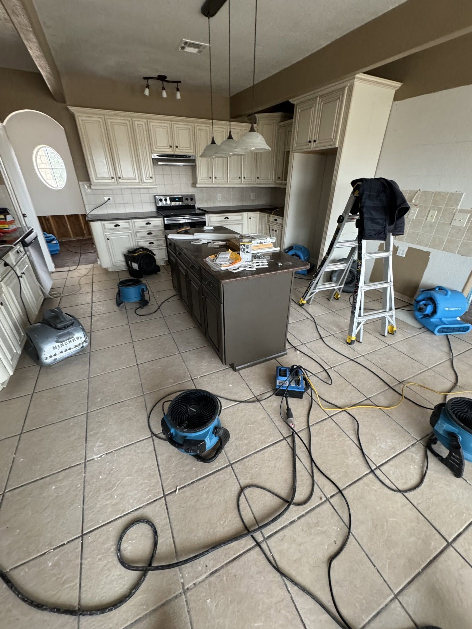 Cluttered kitchen under renovation with tools, cords, and a vacuum on the tiled floor