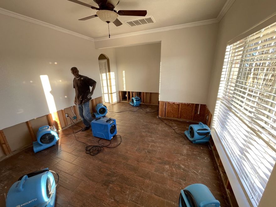 Flood-damaged room with fans, a worker, and standing water on the floor