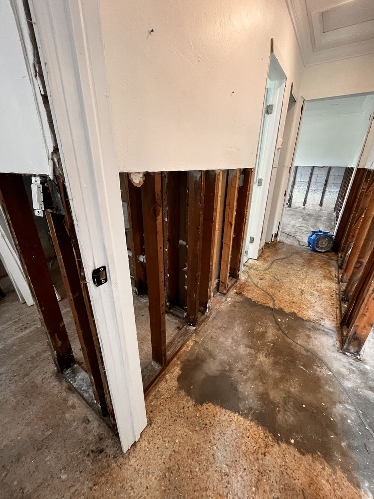 Damaged hallway with exposed wall studs, torn drywall, and debris-covered floor during renovation
