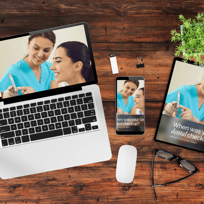 Laptop, phone, and tablet showing a dentist examining a patient; other office items rest on a wood desk.