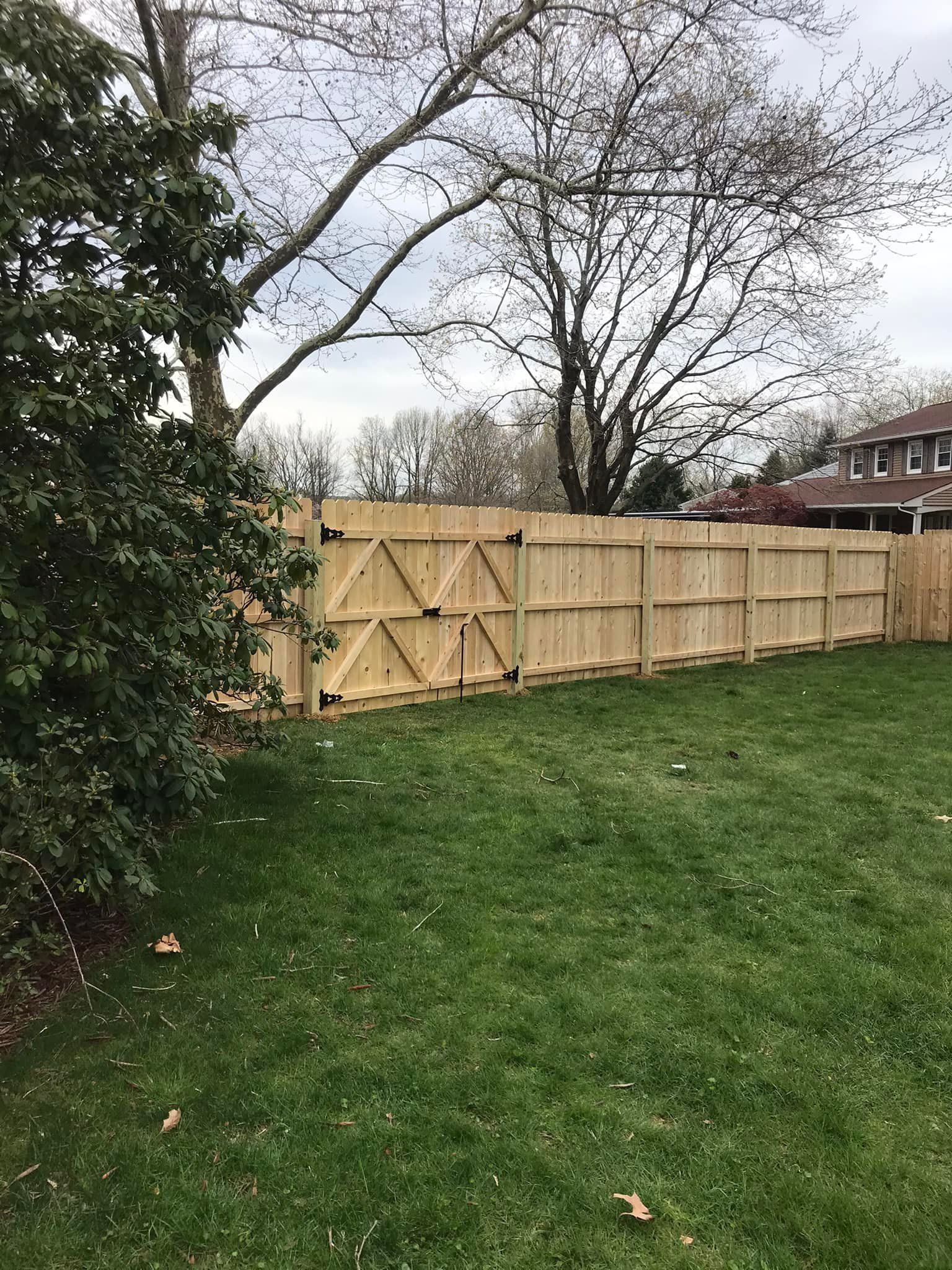 A wooden fence is in the middle of a lush green yard.