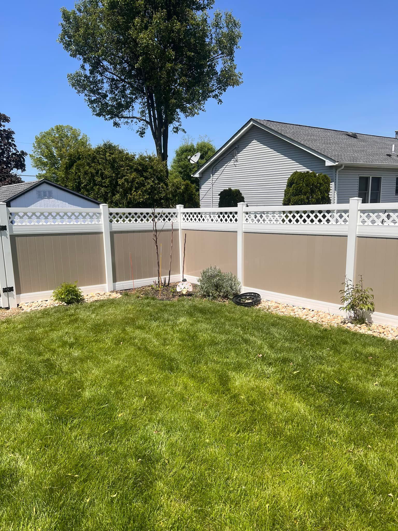 A white fence surrounds a lush green lawn in front of a house.