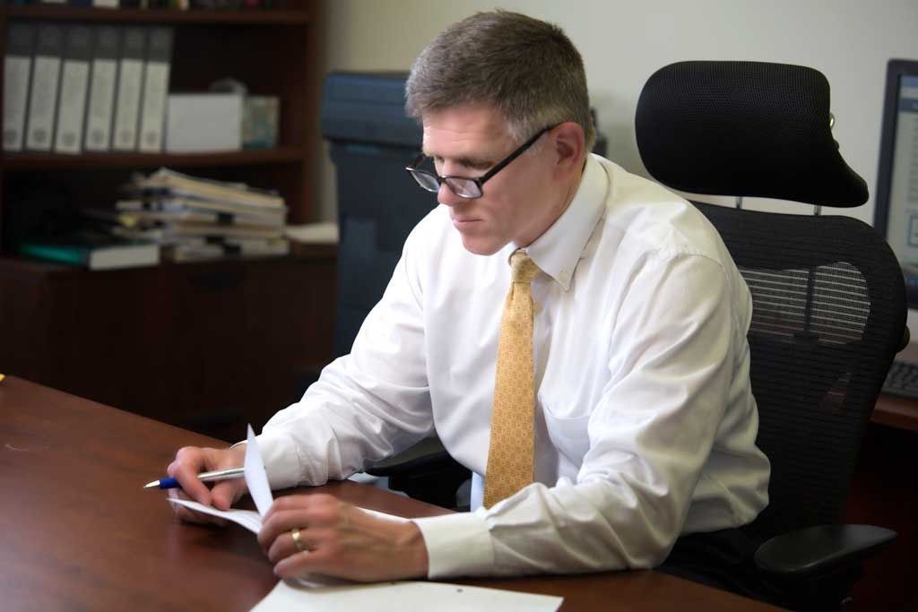 A professional in a white shirt and gold tie sits at a desk, reviewing documents in an office setting.