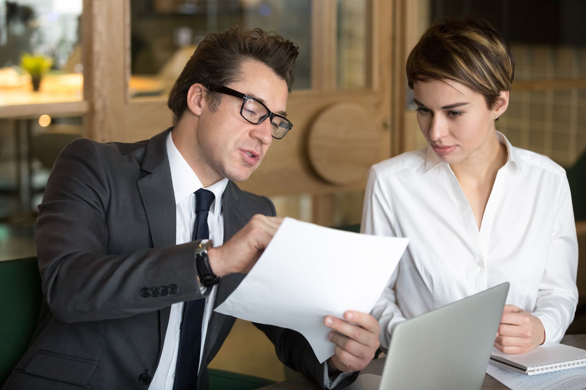 A person in a suit reviews a document with a colleague in an office setting.