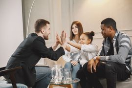 A man gives a high-five to a smiling child seated between two adults in a bright, modern room.