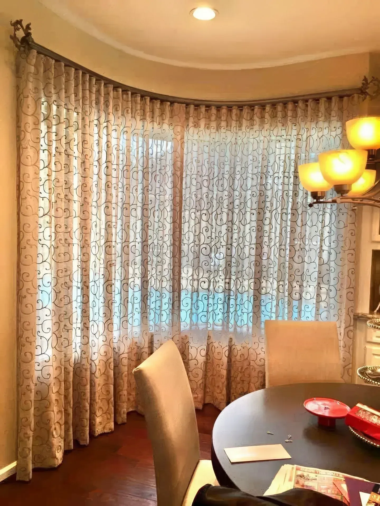 Curved window with sheer, patterned curtains and a dining table with chairs.