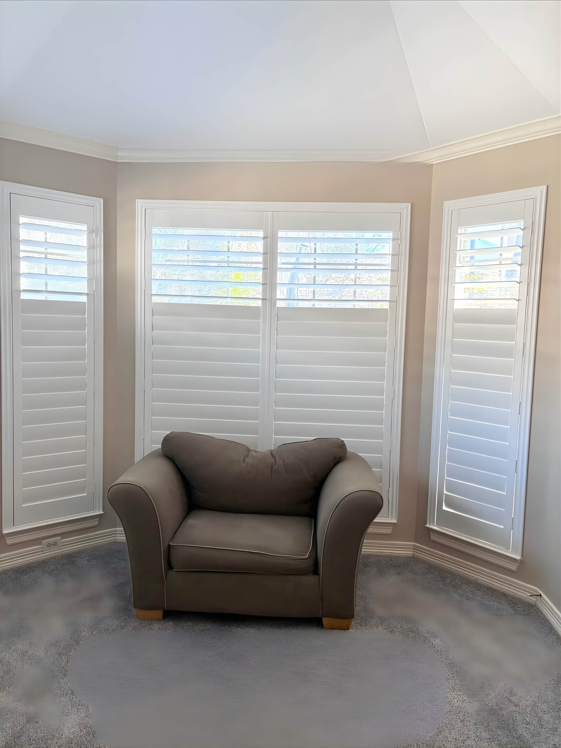 White shutters frame a bay window with a tan armchair on a gray rug.