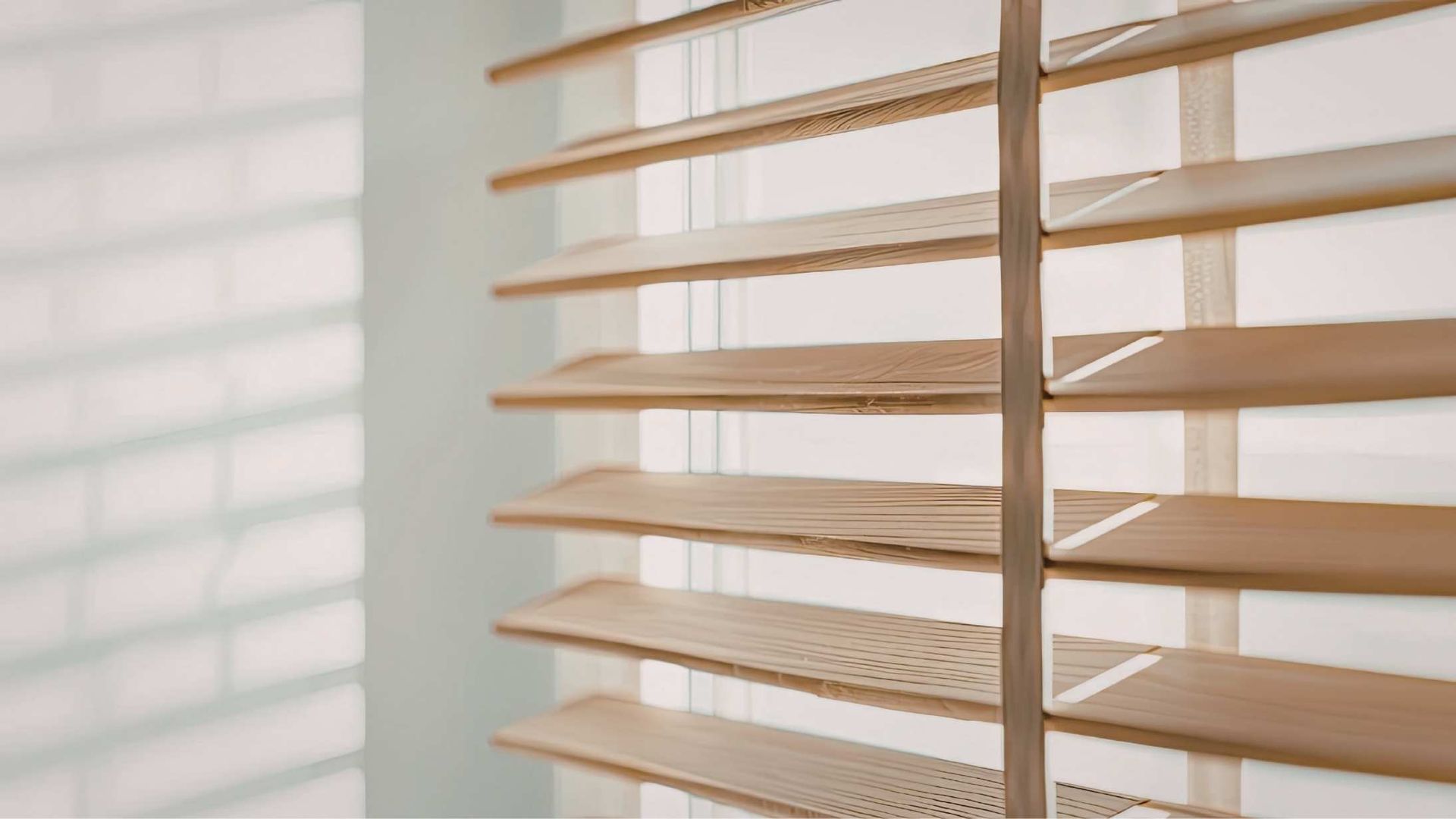 Wooden blinds, slats open, casting shadows on a pale blue wall.