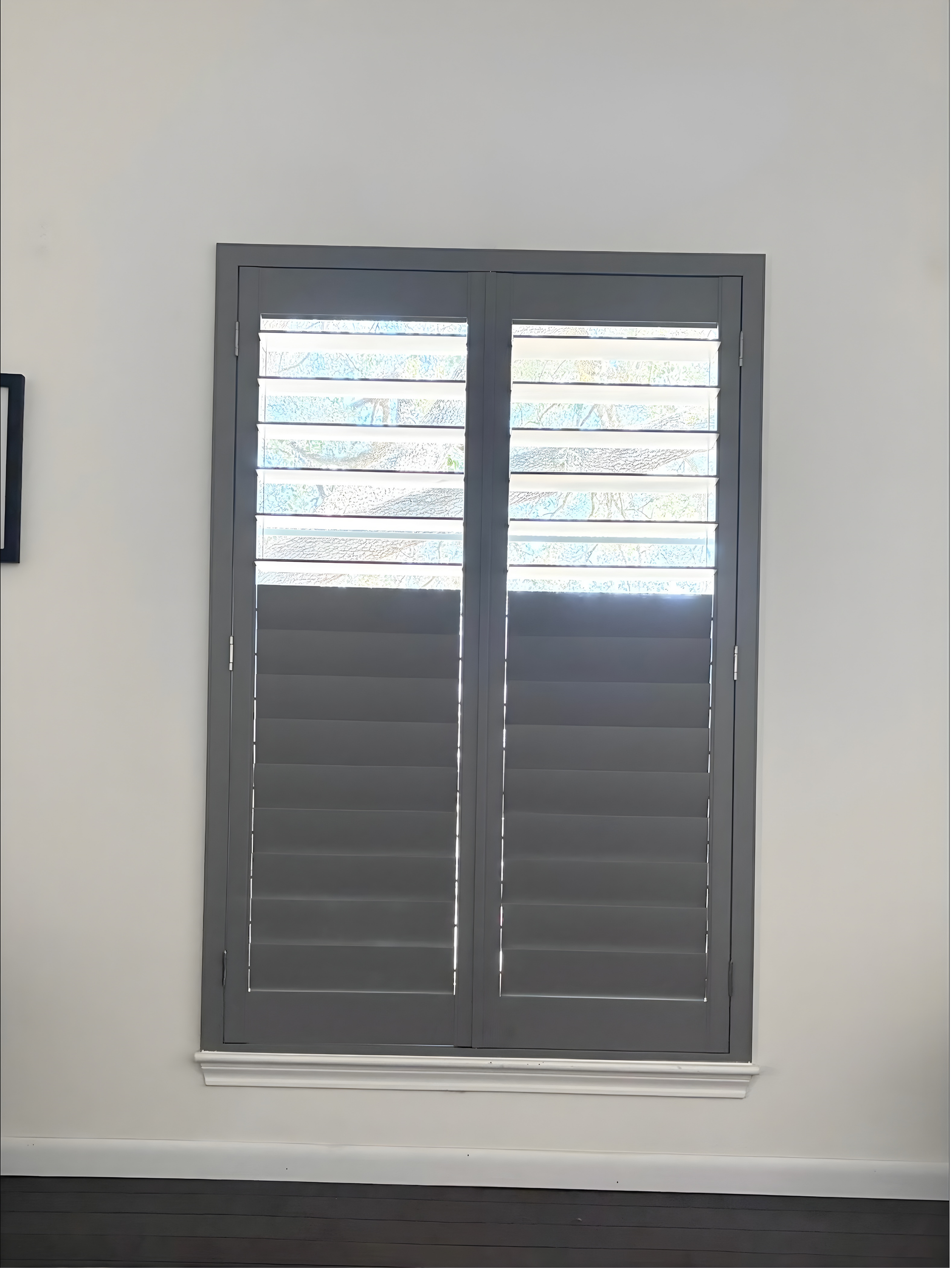 Gray window shutters on a white wall, partially covering a window.