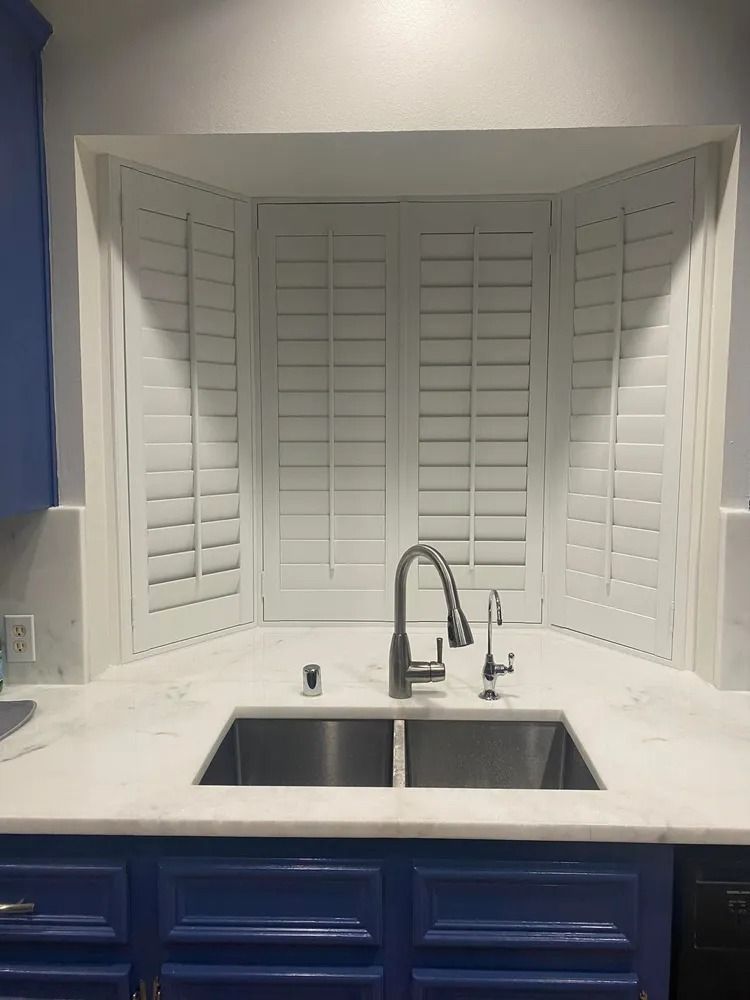 Kitchen sink with white shutters, marble countertop, and blue cabinets.