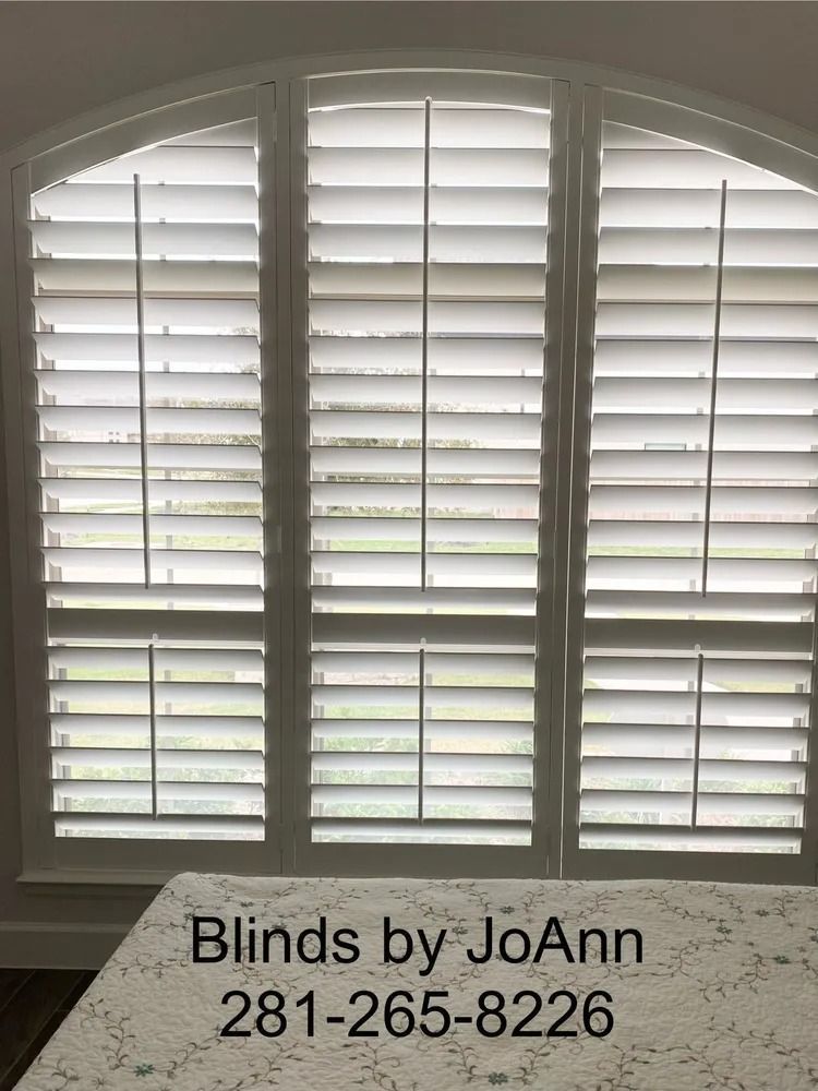White plantation shutters in arched window. Phone number on bottom.