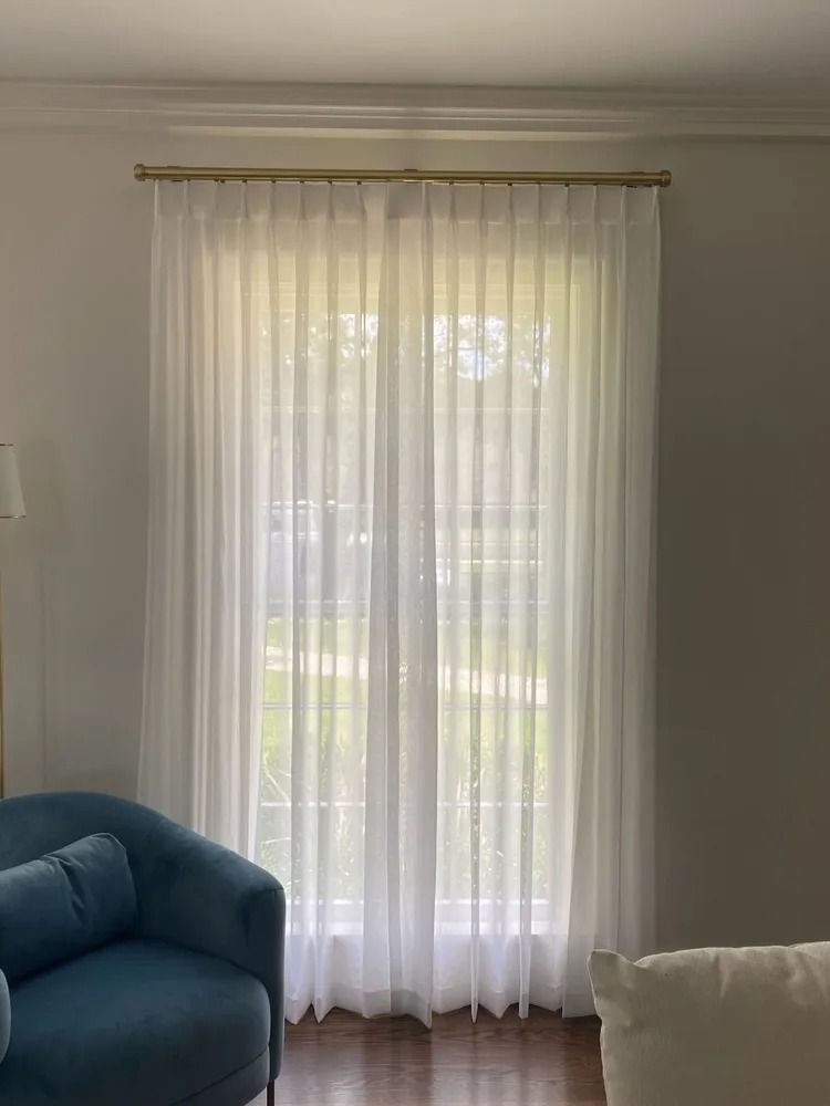 Sheer white curtains covering a large window, blue chair and white pillow visible.