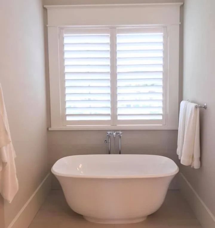 White claw-foot bathtub in a bathroom with shuttered window and towel rack.