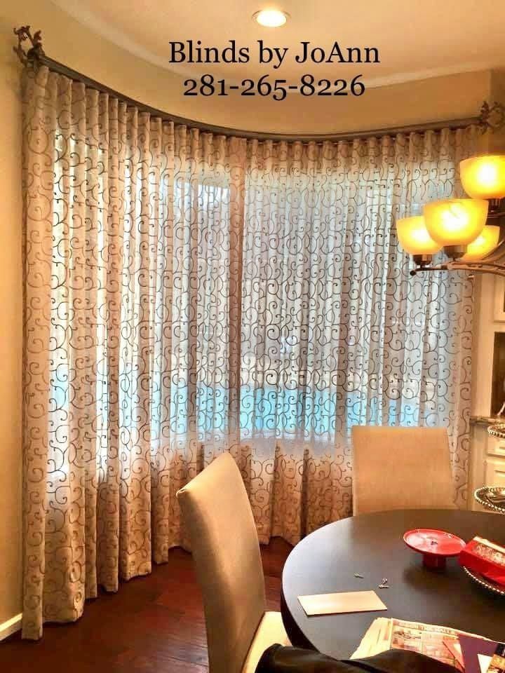 Curved window with sheer patterned curtains, round table, and a chandelier in a dining area.