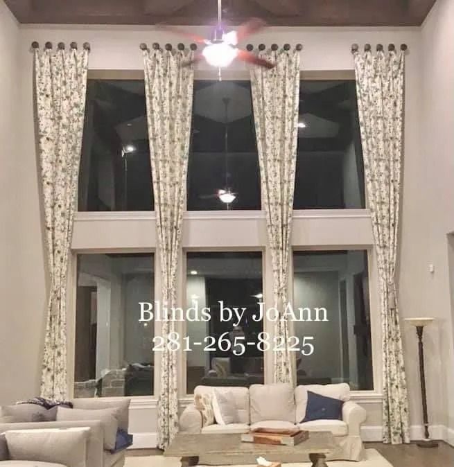 Tall windows with floral drapes in a living room. A sofa and chairs are in front.