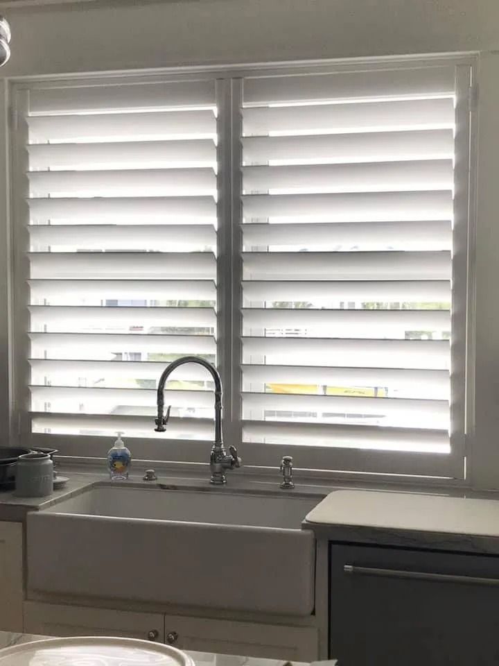 White plantation shutters over a kitchen sink and faucet.