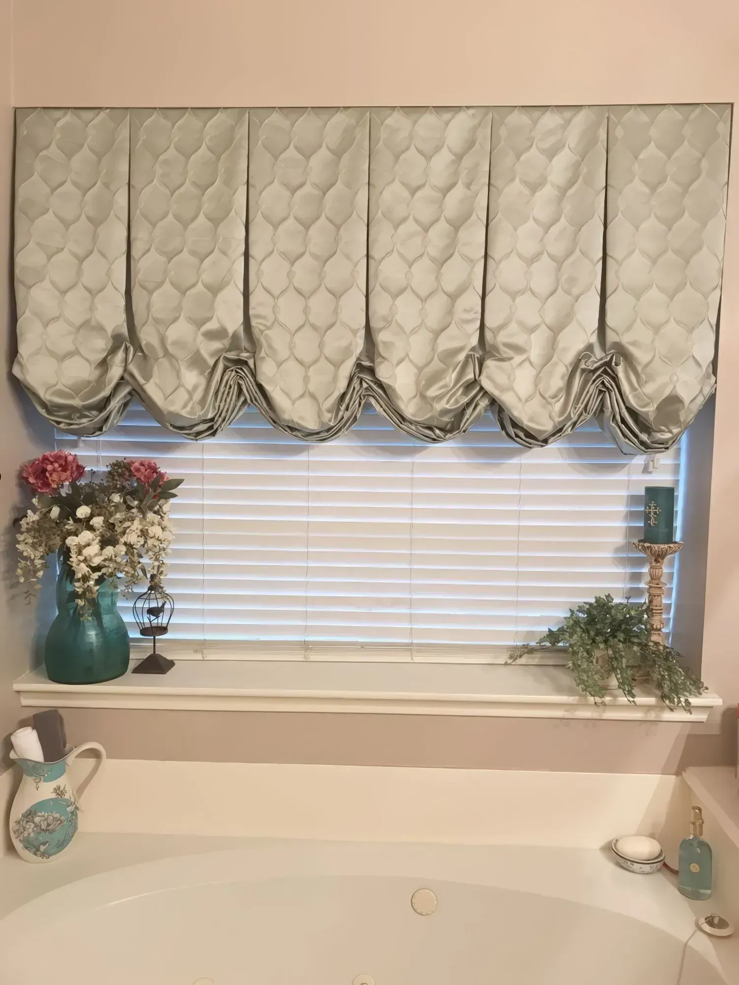 Bathroom window with aqua fabric valance, white blinds, and a bathtub.