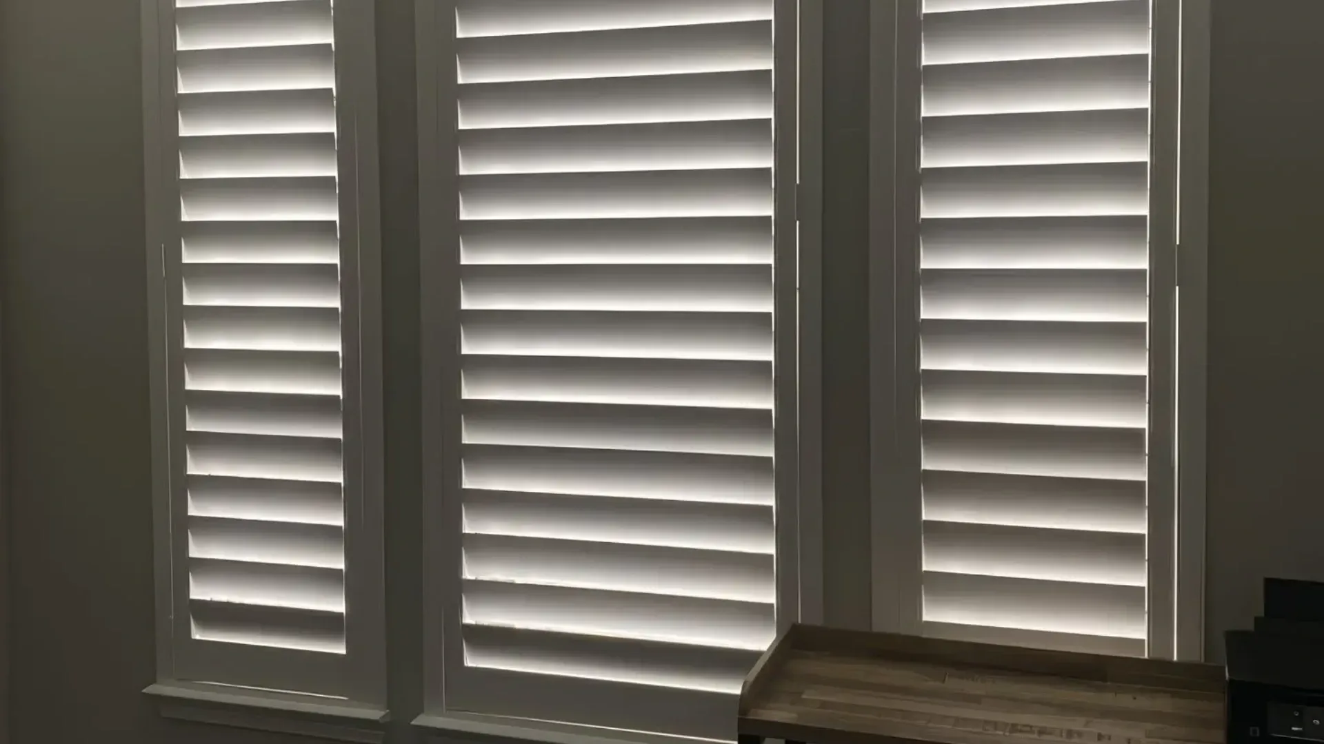 Three white louvered window shutters, angled to filter light in an interior setting.