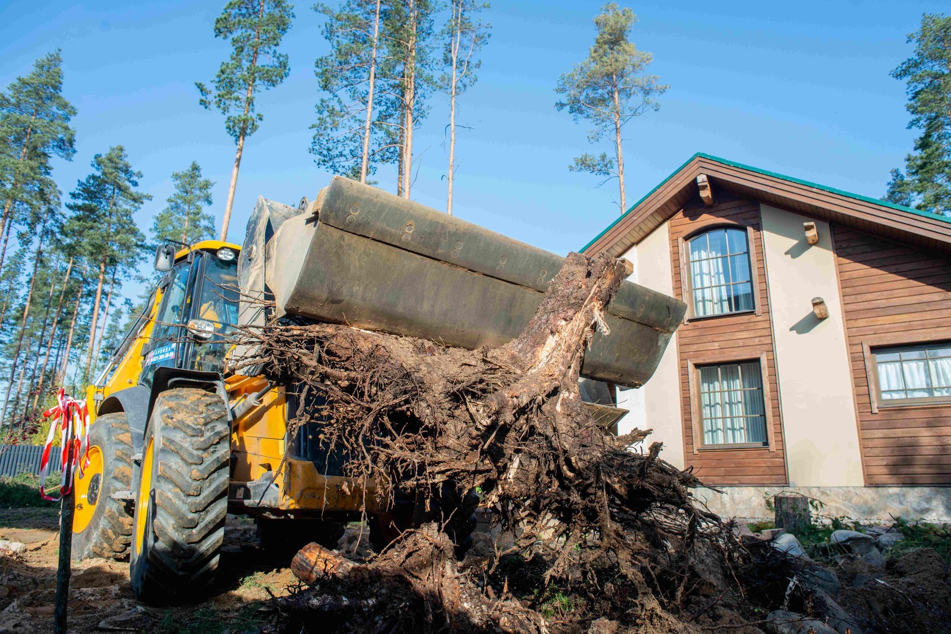 a bulldozer is carrying a large tree stump in front of a house