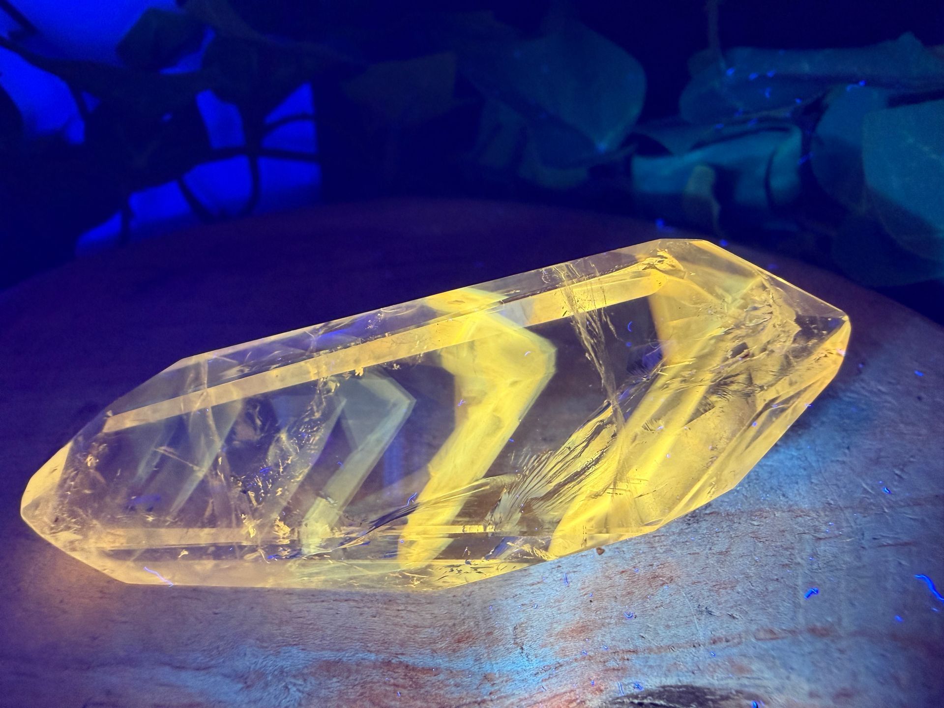 Een geel gefacetteerd kristallen prisma dat oplicht op een donkere ondergrond met blauwe verlichting.