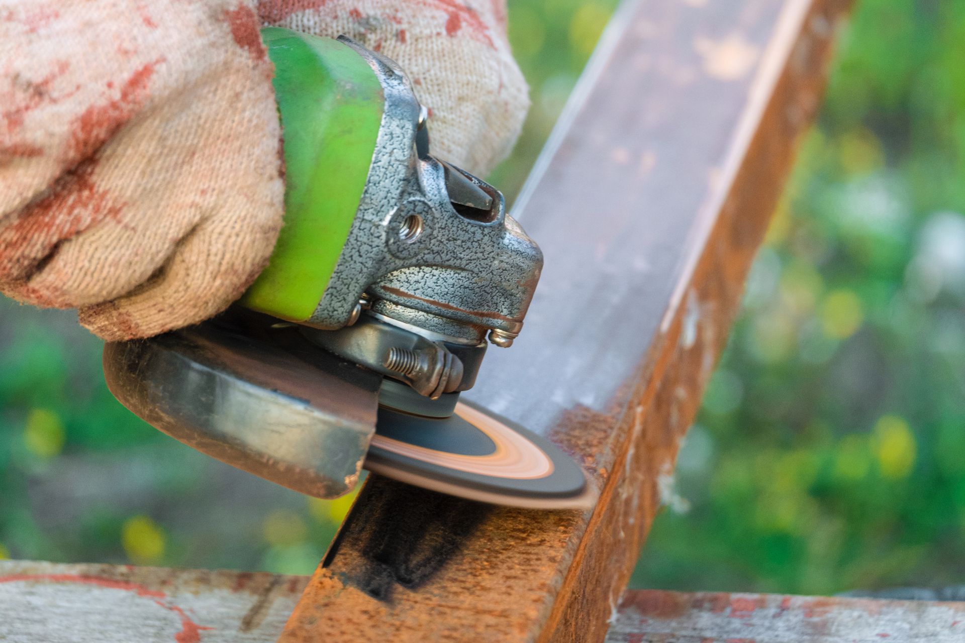 A gloved hand uses an angle grinder on a rusty metal beam outdoors.