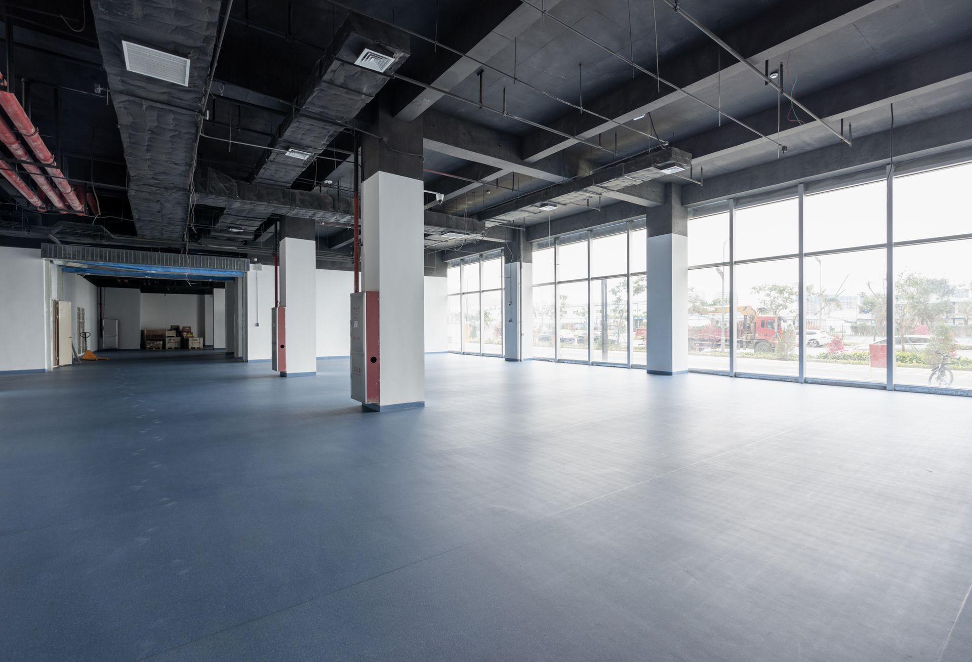 Empty warehouse interior with blue floor, white columns, and large windows.