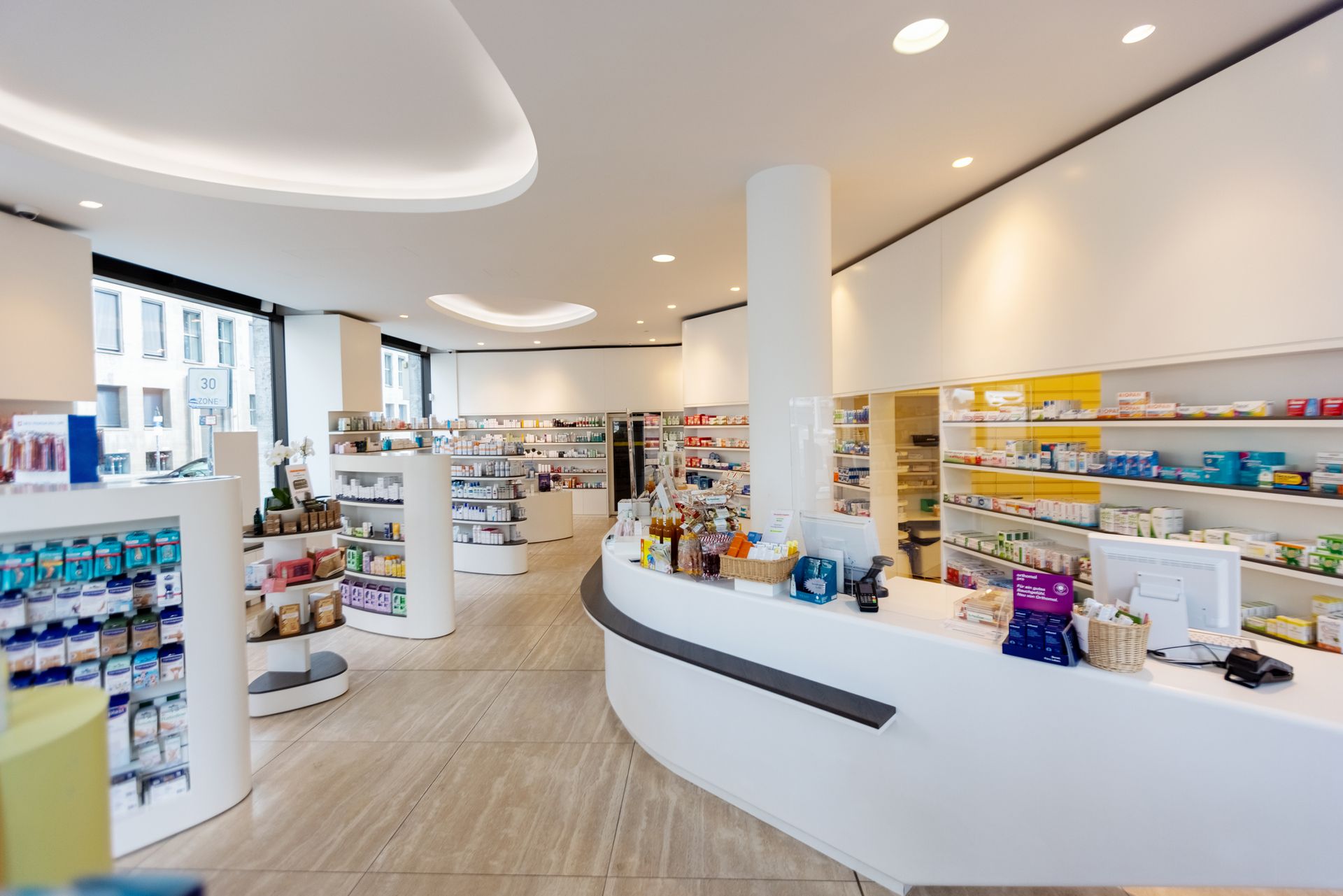 Interior view of a modern, bright pharmacy with white counters, shelving, and products.