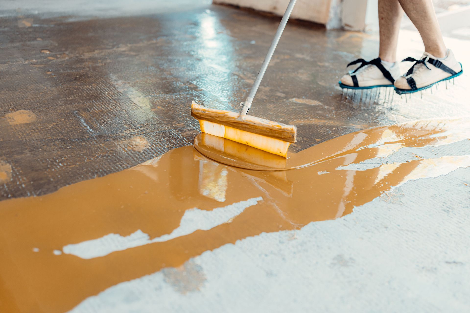 Person using a squeegee to push a brown liquid across a concrete floor.