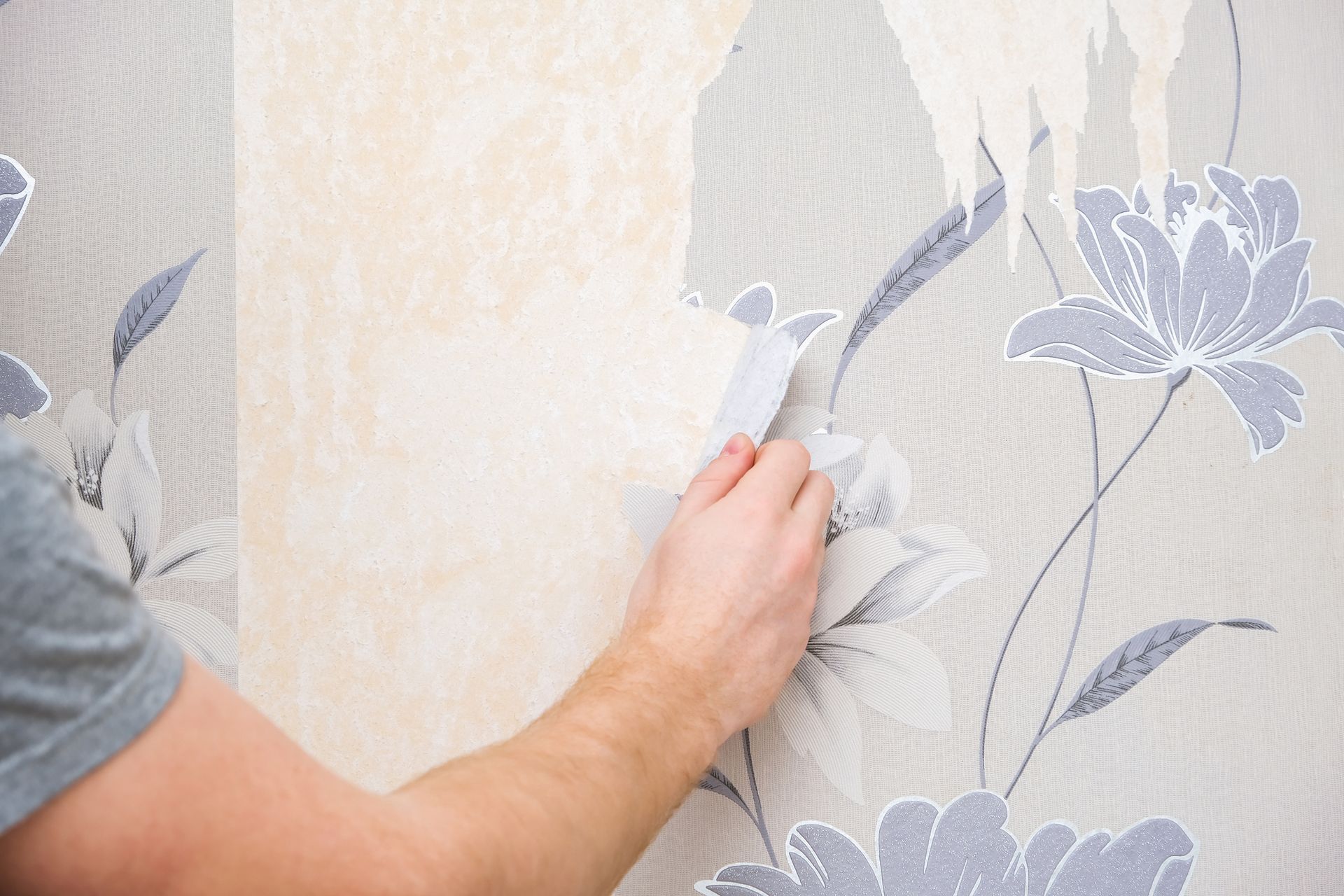 Person peeling floral wallpaper from a wall.