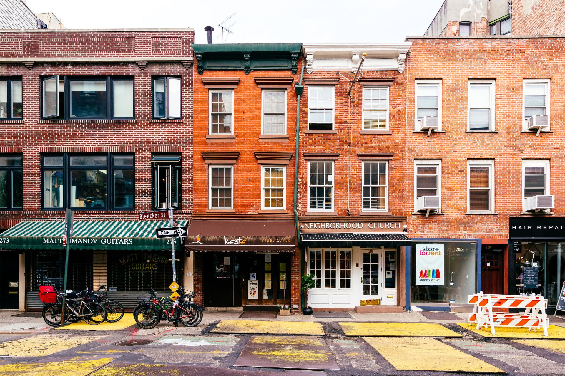 Row of brick buildings with storefronts and parked bicycles along a city street.